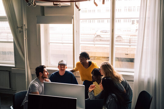 Female tech professional discussing ideas with colleagues on desktop PC in startup office