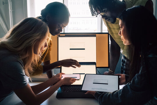 Female and male creative professionals comparing devices while working in tech office