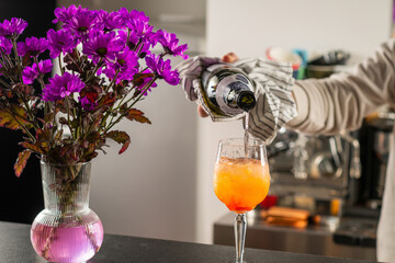 Barman pouring Aperol Spritz cocktail at bar counter. Highlights bubbles, color contrast, and professional cocktail making