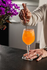 Barista serving Aperol Spritz cocktail at bar counter, decorated with orange slice and ice. Highlights freshness and color balance