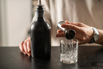 Barman creating gin based cocktail at illuminated bar counter. Focus on clear spirit, ice reflections, and professional presentation