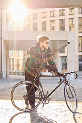 Obraz premium Urban style concept. Young man in stylish jacket and sunglasses dragging bicycle through city