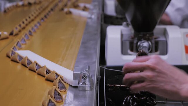 Conveyor belt carrying rows of chocolate-coated triangular pralines with worker operating machinery.