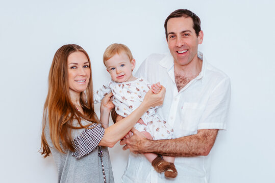 mom and dad happily holding up a baby boy in white background