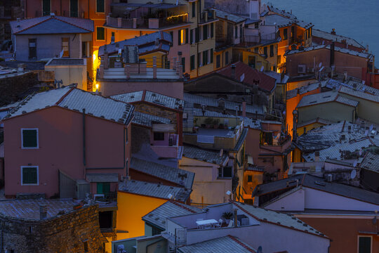 View of colorful buildings stacked upon each other in a maze of rooftops and glowing windows, nestled by the sea, Vernazza, Liguria, Italy.