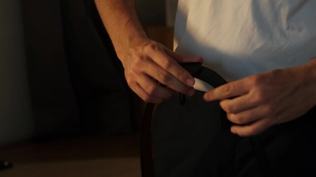 Static shot of a young man demonstrating the adjustment and locking of a leather ratchet belt, lifestyle fashion