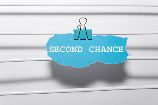 A blue paper with the words 'SECOND CHANCE' clipped to a white surface. The background is simple and minimalistic, emphasizing the message.