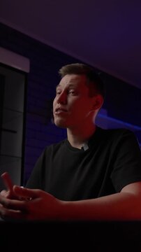 White Creator In Studio Explaining Script For Vlog, Seated At Black Table Under Red And Blue LED Lights, Hands Gesturing, Calm Tone, CameraFacing Monologue And Storyboard Notes Visible