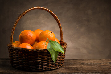 Naklejka premium Bunch of ripe fresh orange fruits in a wicker basket on wooden table.