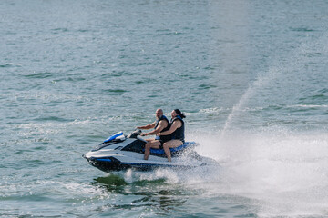 Two individuals riding a jet ski on a body of water, splashes of water visible as they speed across the surface under a clear blue sky