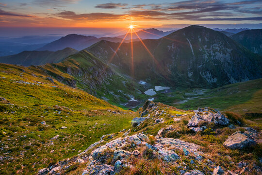 View of radiant sunlight bathes jagged peaks and verdant slopes, painting the sky with fiery hues above serene lakes in Western Tatras, Zilina Region, Slovakia.