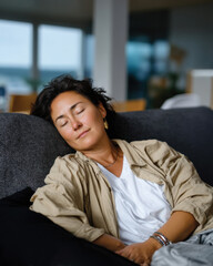 Obraz premium A relaxed woman enjoys a restorative moment, napping on a cozy sofa, embodying tranquility and the necessity of self-care in a busy life.