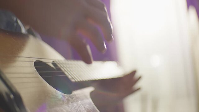 guitarist breaks guitar string, close-up. white male fingerstyle guitarist plucks the strings over sound hole, soft window light and light dust specks, precise technique, and textured wooden surface