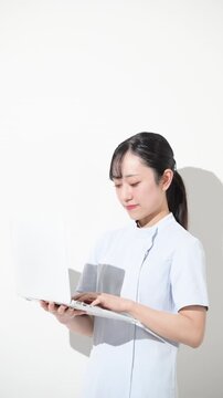 白色背景でパソコンを持つタイピングする看護師　転職や採用などのイメージの縦動画　最後にカメラ目線
