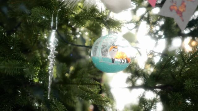 A sparkling glass ornament featuring a fox hangs on a Christmas tree. The intricate design and glowing lights create a magical and cozy holiday atmosphere.