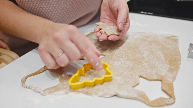 A close-up of hands using cookie cutters to shape gingerbread dough on a floured countertop. The scene captures the warmth and creativity of seasonal baking