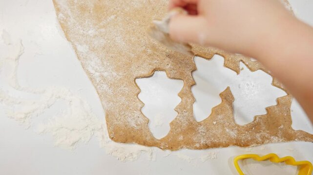 A toddler helps cut festive shapes from gingerbread dough using cookie cutters. The floured surface and creative activity capture the warmth of holiday baking traditions.