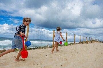 Happy kids run on beach walk with shovels and bucket near ocean