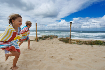 Children have fun run to sandy beach wrapped in towels on summer