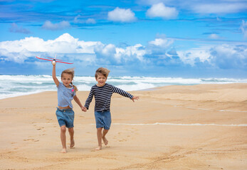 Happy kids run on sandy beach with a toy airplane, hold hands