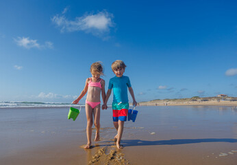 Children walking on beach holding buckets search shells in sand