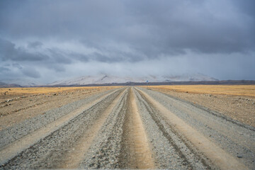 Gravel road stretching from Altai towards the Mongolian border with snowy mountain ridge. Desert...
