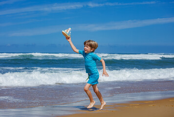 Young boy joyfully run on beach with toy sailboat at vacation