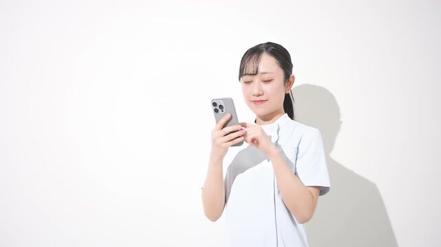 スマホを持つ女性看護師カメラ目線　転職や採用などのイメージ　スマホを見る、タップする就活先や転職先を探す、検索する動画	