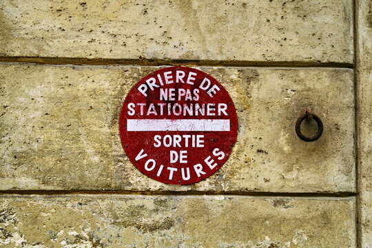 Pri&egrave;re de ne pas stationner. Sortie de voiture. Inscription sur panneau rond rouge et blanc de sens interdit sur mur de pierre.