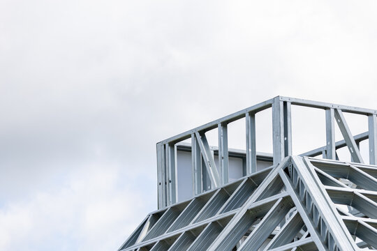 Close-up of a modern galvanized light steel frame LSF construction. Architectural details of roof trusses and wall framing against a blue sky. A sustainable and efficient building material.