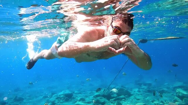 man in sea on face snorkelling mask show by hands heart big love and declaration of love, after two thumbs up super. trip into water all underwater world to see fish in vacation
