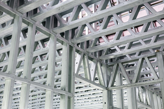 Close-up of a modern galvanized light steel frame LSF construction. Architectural details of roof trusses and wall framing against a blue sky. A sustainable and efficient building material.