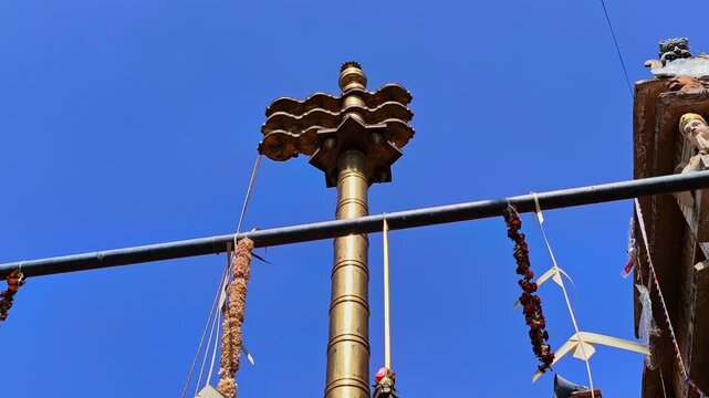 Brass Dwajasthambam (Temple flag pole) with Temple gopuram and background blue sky at kodangal, india. day time, low angle shot, stable shot, 4k.