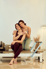 Friends Share Warm Hug During Pilates Reformer Session in Bright Studio
