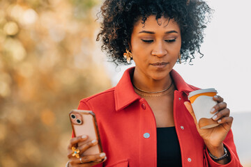 young latina woman on the street with a cell phone and a cup of drink