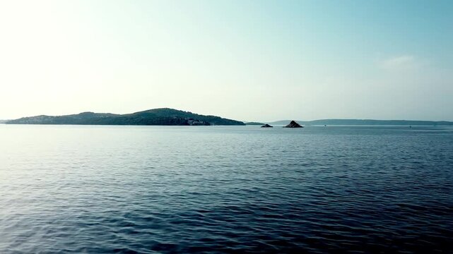 Calm Adriatic seascape with low islands on horizon under clear sky, peaceful ocean backdrop, Seget Vranjica Croatia