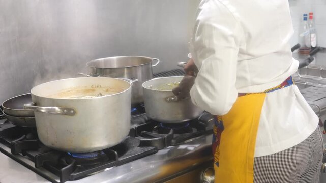 Slow motion view of chef stirring simmering sauce, veloute soup or risotto in stainless pots on a gas range, showing professional meal preparation, heat control, and commercial kitchen cooking.