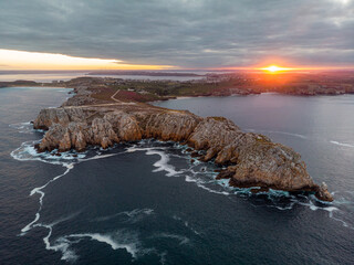 Aerial view of the rugged cliffs and rocky headlands of Pen Hir at sunset, with warm golden light over the Atlantic Ocean creating a dramatic coastal landscape in Brittany, France.

