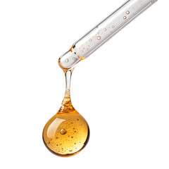 Golden liquid dropping from a glass pipette on white background