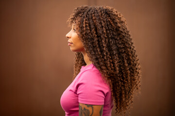 Profile portrait of an African American woman with curly hair against brown wall © Paula