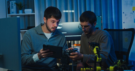 Team adult male engineer collaborate on robotic hand project using AI code solutions machine learning at tech workspace night. Artificial intelligence interface, collaboration prototype development.