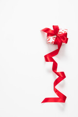 Vertical composition with a small Valentine's Day gift box wrapped in paper with a red kiss print and tied with a long red satin ribbon on a white background, with space for text.