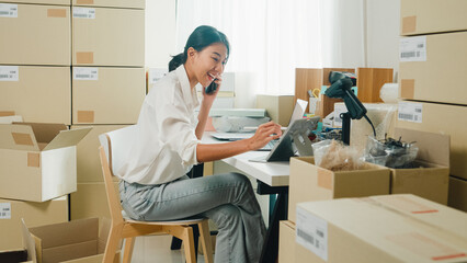 Youth attractive Asia female entrepreneur small business start up call smartphone confirm order with customer confirm check stock inventory product ready for delivery shipment at online retail shop.