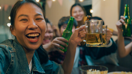 Closeup Group of diversity adult Asia people use phone greeting friend on remote video call hangout party at dining table in night life indoor home. Happy hour millennial generation inside house.