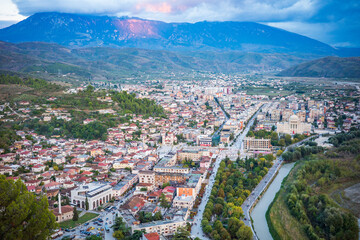 Obraz premium A stunning aerial view of a vibrant European city nestled in a wide valley, featuring a long tree-lined boulevard, winding river, dense urban neighborhoods, and dramatic mountains