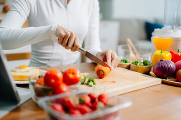 Close up of woman cutting fresh carrot in home kitchen. Healthy cooking, clean eating, nutrition, meal prep and vegetarian lifestyle with organic ingredients.