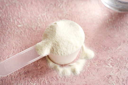 Collagen powder in a measuring scoop on pink background