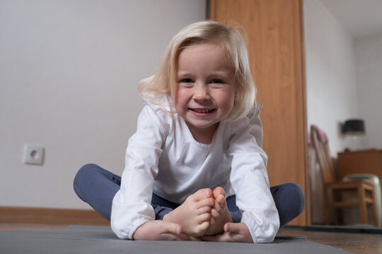 Little girl practicing yoga in Butterfly pose Baddha Konasana at home.