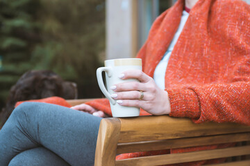 A woman holds a cup of hot drink in a cozy atmosphere. Nearby sits a dog