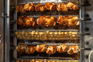 A commercial rotisserie oven at a market stall in Spain cooking whole chickens and potatoes at the same time. The potatoes are placed below the rotating chickens to collect drippings during cooking